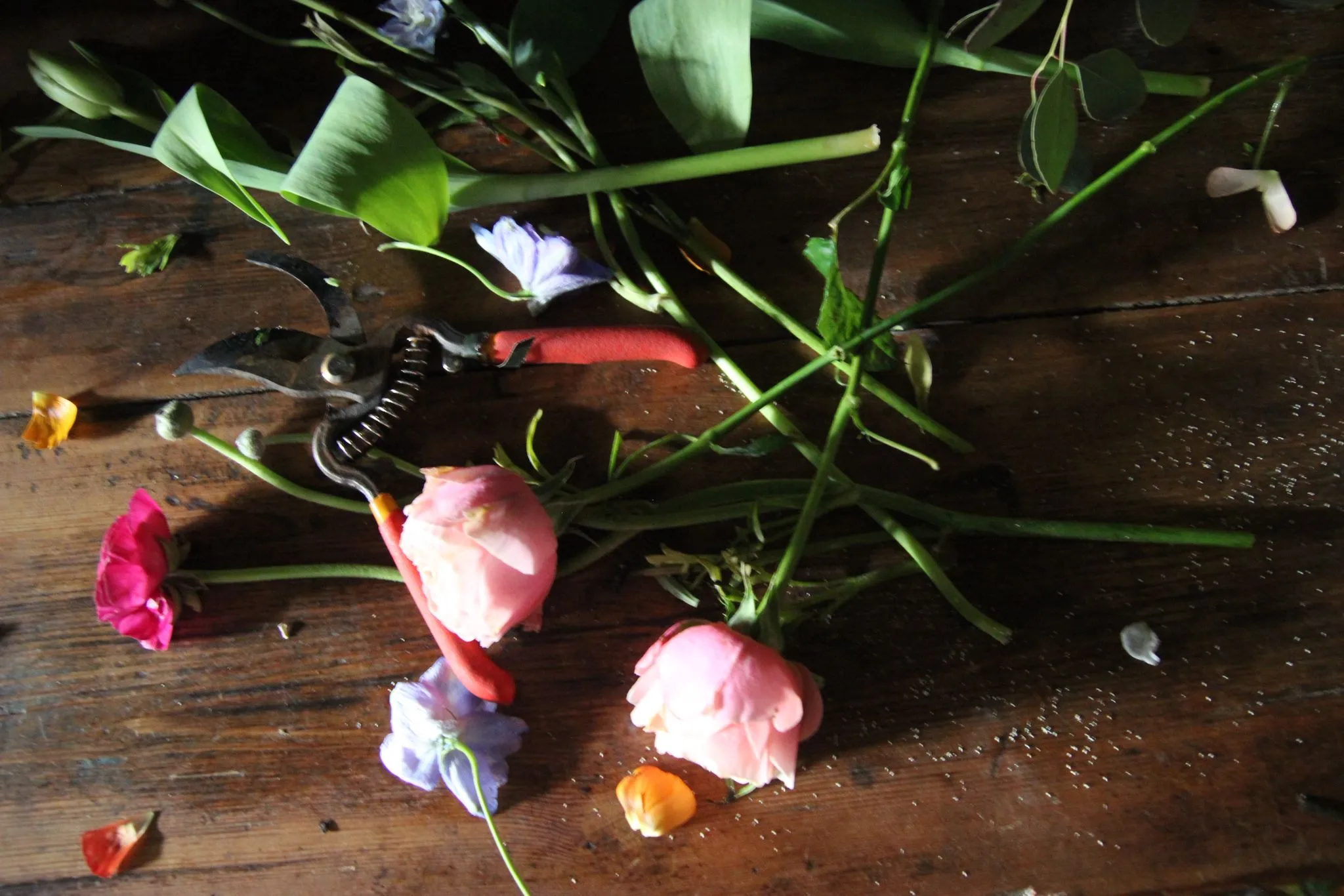 Olivia Baglivi de perfil componiendo un ramo, con flores dispersas sobre la mesa a su alrededor